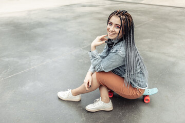 Extraordinary female millennial skater with colorful makeup, African braids in a skate park. Youth, lifestyle concept