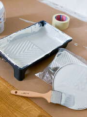 Painting utensils. Brush, masking tape, paint bucket, panit roller tray. On paper drop cloth. Grey paint color.