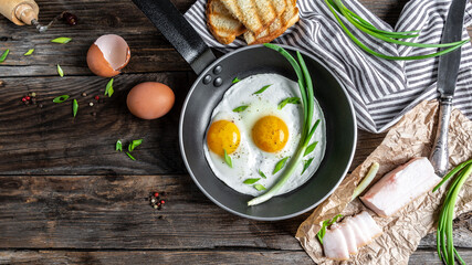 breakfast or brunch fried bacon and eggs in black skillets and crispy toasts top view