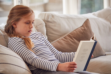 Obraz premium Young Girl Relaxing On Sofa At Home Reading Book