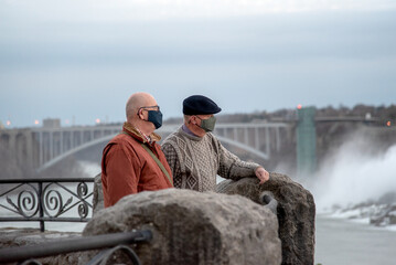Senior Caucasian gay married couple wearing face masks enjoy their visit to Niagara Falls, Ontario,...