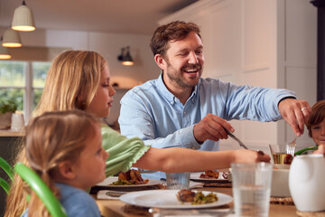 Family Sitting Around Table At Home Enjoying Meal Together