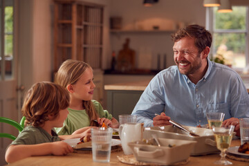 Father And Children Sitting Around Table At Home Enjoying Meal Together