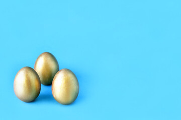 Easter eggs on blue background. Three golden eggs. Minimal style. Easter decorations.