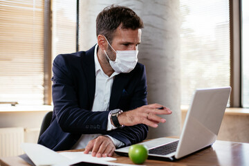 Young businessman with a mask working in his office on laptop. COVID - 19 virus protection