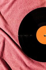 Flat lay of LP vinyl record on a pink fabric cloth background.  Old vintage record.
