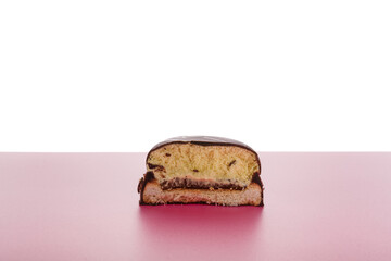 Half of biscuit cookie in chocolate glaze or frosting with jam inside on pink background. Sweet tasty unhealthy snack. Copy space.