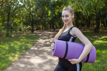 Slim fit young healthy woman with yoga mat in hands in the park. Active lifestyle. Outdoor workout