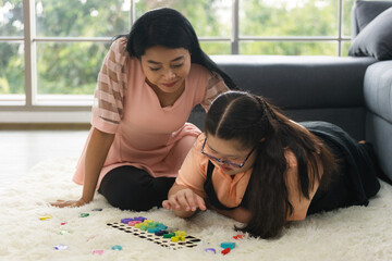 young girl with autism is practicing playing with toys on the floor at home with his mother. Autistic young students are learning with teachers.