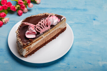 Half of cake on white plate on blue painted background. Sweet bakery with artificial spring flowers