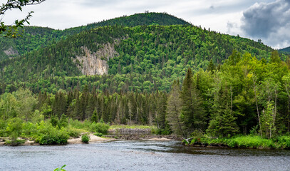 Fototapeta premium Huge cliffs with green trees everywhere on it facing two dams made by beavers near Fjords du Saguenay in Quebec Province, Canada
