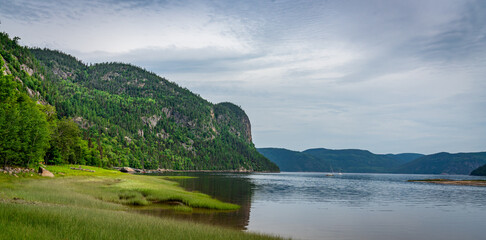 Huge cliffs flowing down into the sea in Fjords du Saguenay, Quebec Province, Canada,at Notre-Dame-du-Saguenay track with sailing boat on the foreground during a cloudy day