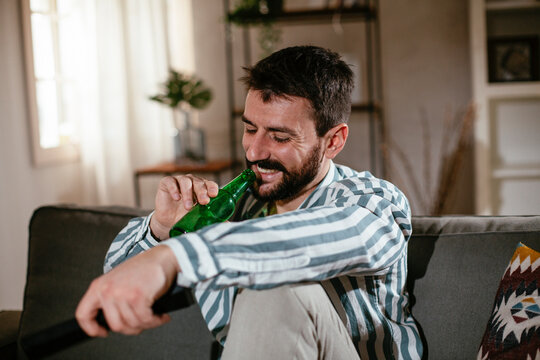 Young man at home. Man sitting in living room watching movie and drinking beer..