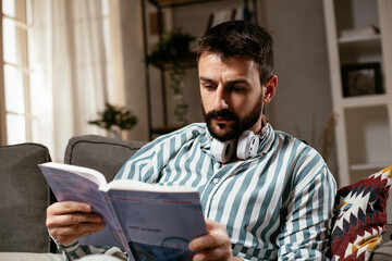 Man at home studying. Young man reading a book on the couch
