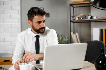Fototapeta premium Young businessman working on laptop at office. Businessman sitting at office desk working on new project.