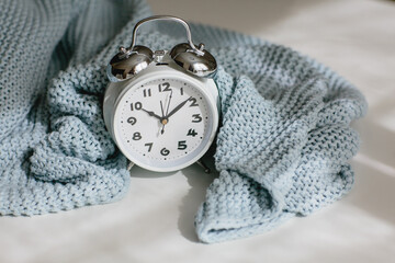 Gray knitted plaid and alarm clock on a white background. Seasonal time change, daylight saving time concept.
