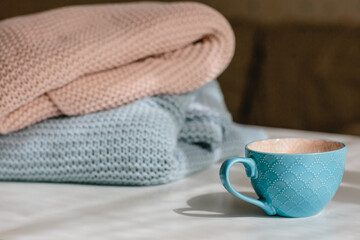 Gray and pink knitted blankets and a blue cup on a white background. Seasonal time change, daylight saving time concept. Horizontal image.