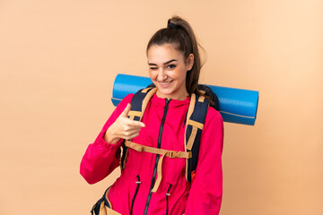 Young mountaineer girl with a big backpacker isolated on beige background points finger at you