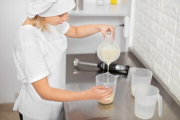Cooking, baking and people concept. Young woman, professional confectioner, working in the kitchen, preparing the sauce or ganache for desserts, pouring cream from one cup to another