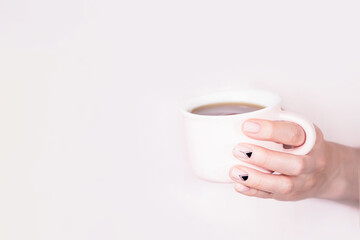 Hand holding pink cup of black tea on pale pink background, copy space