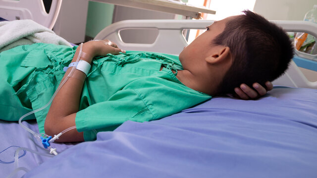 Side View Of Sick Boy Lying On Bed In Hospital Ward