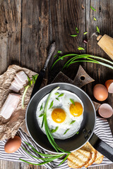 Delicious breakfast or snack scrambled eggs in frying pan with pork lard, bread and green feathers onions, vertical image