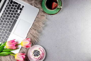  A cup of tea, tulips and a cake next to a laptop on the table. Cozy work from home concept in spring, top view