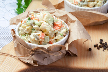 
a portion of Olivier salad with chopped pickles, vegetables, served on a white plate on a cutting board. Spices on the background. View from above