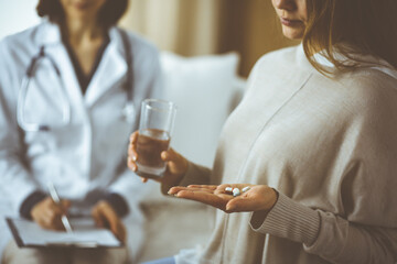 Close-up woman-patient holding pills near her doctor, time to take medications, cure for headache or remedy pain killer drugs. Stay at home concept during Coronavirus pandemic and self isolation