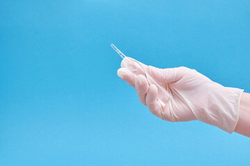 Ampoule with a medicine or vaccine and a syringe in hands in rubber gloves on a blue background
