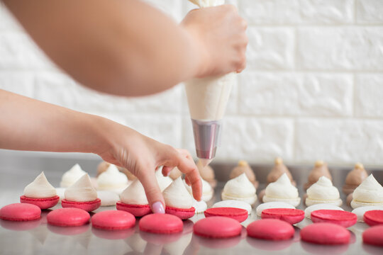 Step by step process of making macarons in confectionery shop. Close up horizontal shot of macarons shells in rows and hands of female pastry chef, filling it with white cream ganache