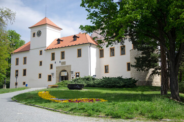 Fototapeta na wymiar Castle in Moravský Kras, Czech Republic, White building with red roof, green grass with flower bed, tree, path