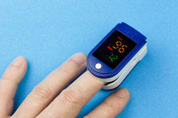 Oximeter on the finger of a man's hand on a blue background.