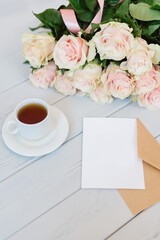 White blank card for text on a craft envelope with a bouquet of roses on a light background.