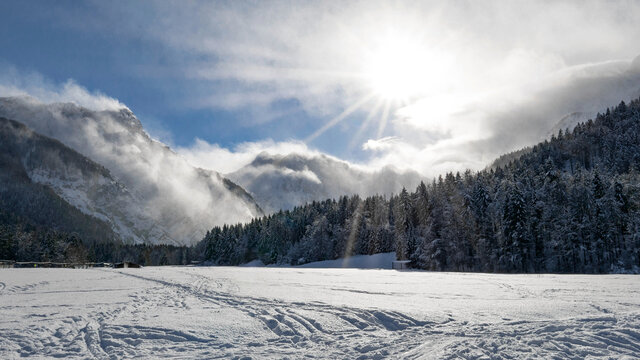Snow covered plain surrounded by mountains and forests. Sunny winter day. Ratece, Slovenia