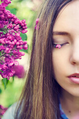 Spring portrait of young woman with lilac petals on eyes. Girl with lilac flowers in springtime. Gardening, aromatherapy, spring concept. Vertical image.