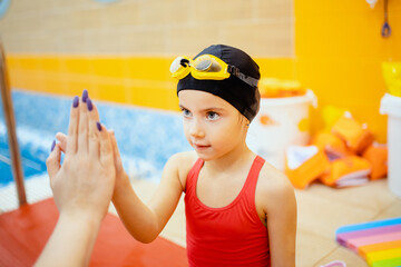 Coach gives hand five to child girl, concept of teaching children to swim in pool