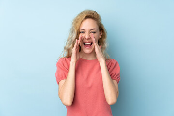 Young blonde woman isolated on blue background shouting with mouth wide open
