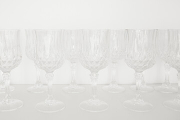 Dishes in kitchen. Transparent glass wineglasses, stand in row on white shelf in kitchen cabinet. 