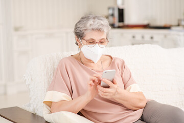 A pretty retired old woman with a medical mask during a coronavirus lockdown calls up with relatives via video chat using a phone. Quarantine during coronavirus pandemic concept