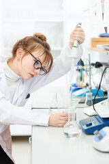 In a chemical laboratory, a girl laboratory assistant drips a solution into a measuring beaker with a special pipette