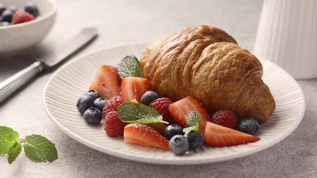 Croissant with berries and mint on a plate, delicious breakfast. The camera moves along, close-up 
