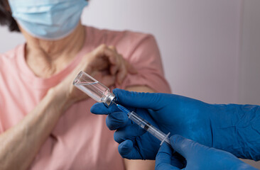 Elderly asian woman is vaccinated against Covid-19 Doctor draws a dose of vaccine into a syringe....