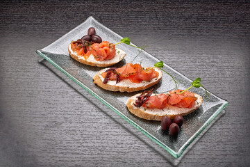 Bruschetta with trout, salmon, cream cheese and microgreen on a glass plate on a dark background