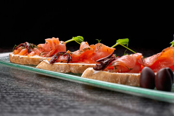 Bruschetta with trout, salmon, cream cheese and microgreen on a glass plate on a black background