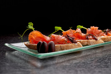 Bruschetta with trout, salmon, cream cheese and microgreen on a glass plate on a black background