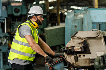 Male engineer is looking at the machine while he is using the tablet to check quality of the...