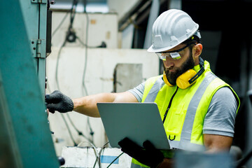 Mechanical engineer is setting up the control panel and looking the system in the laptop to check security in the control room at the factory.