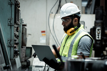 The engineer is checking and inspecting at the factory. He is working with the laptop to check...