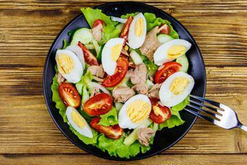 Tasty tuna salad with eggs, lettuce and fresh vegetables on wooden table. Top view